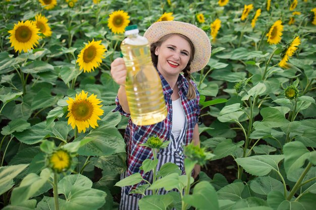 Zdjęcie piękna, uśmiechnięta, radosna kobieta w średnim wieku, trzymająca w dłoniach butelki złotego oleju słonecznikowego na polu żniw słoneczników w słoneczny dzień