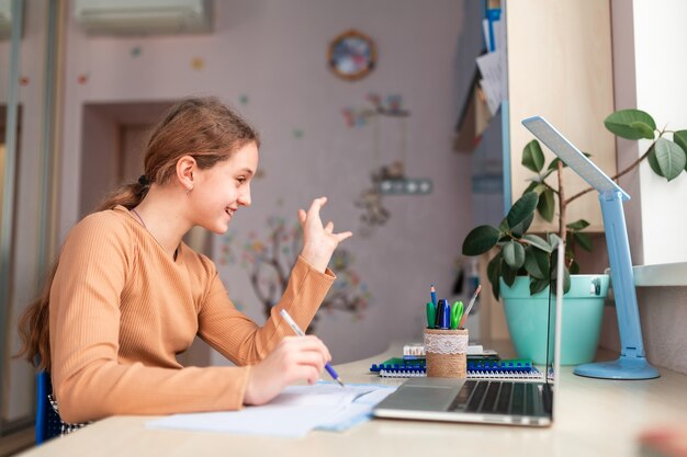 Piękna uśmiechnięta uczennica studiuje w domu odrabianiu lekcji w szkole. Książki szkoleniowe i notatnik na stole. Edukacja online na odległość