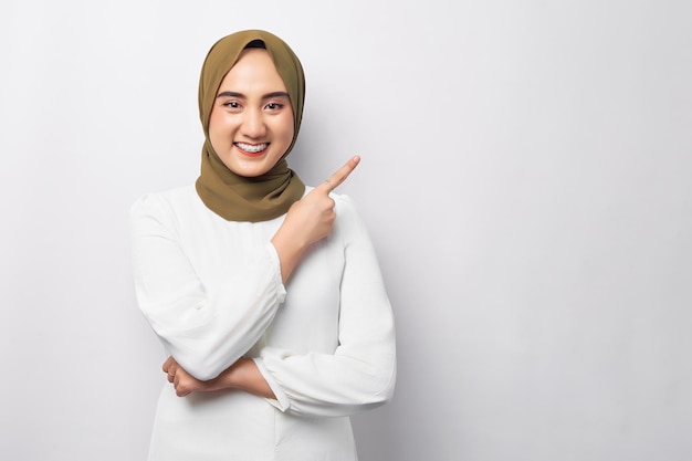 Piękna, wesoła młoda arabska muzułmańska kobieta ubrana w hidżab wskazująca palcem na puste miejsce na kopię odizolowana na białym tle Koncepcja religijnego stylu życia ludzi