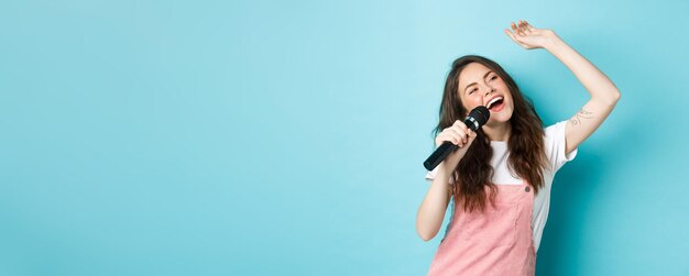 Zdjęcie piękna wokalistka trzymająca mikrofon śpiewająca karaoke w mikrofonie stojąca na niebieskim tle