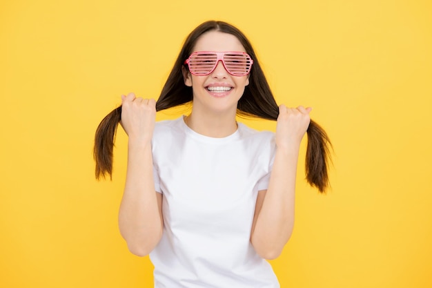 Piękna zabawna nastolatka z imprezowymi okularami na żółtym tle Zaskoczona młoda kobieta w zabawnych okularach