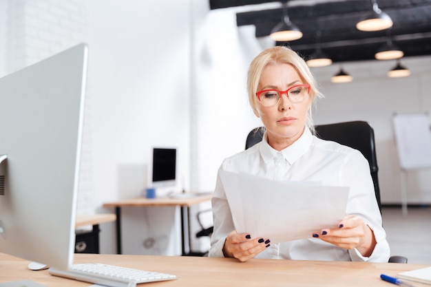 Zdjęcie piękna zamyślona dojrzała kobieta czytająca dokumenty w biurze
