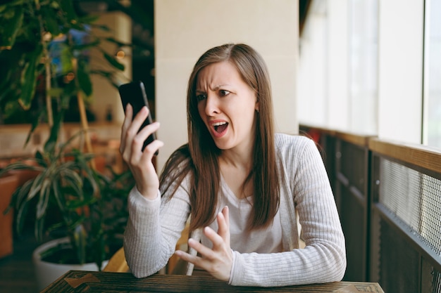 Piękna Zdenerwowana Kobieta Siedzi Samotnie W Pobliżu Dużego Okna W Kawiarni, Relaks W Restauracji W Czasie Wolnym. Smutna Kobieta Po Rozmowie Z Telefonem Komórkowym, Odpoczynek W Kawiarni. Koncepcja Stylu życia.