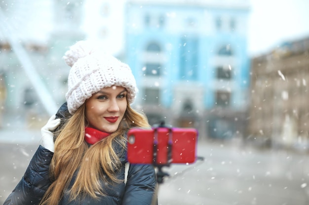 Piękne blond kobieta z długimi włosami przy selfie na centralnym placu miasta podczas opadów śniegu. Pusta przestrzeń