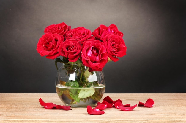 Piękne czerwone róże w wazonie na drewnianym stole na szarym tle
