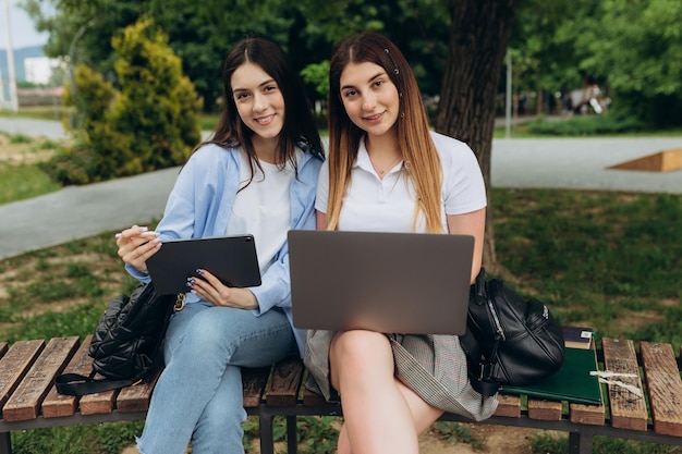 Piękne dwie młode dziewczyny pracują i uczą się za pomocą gadżetów Uczniowie używają laptopa i tabletu