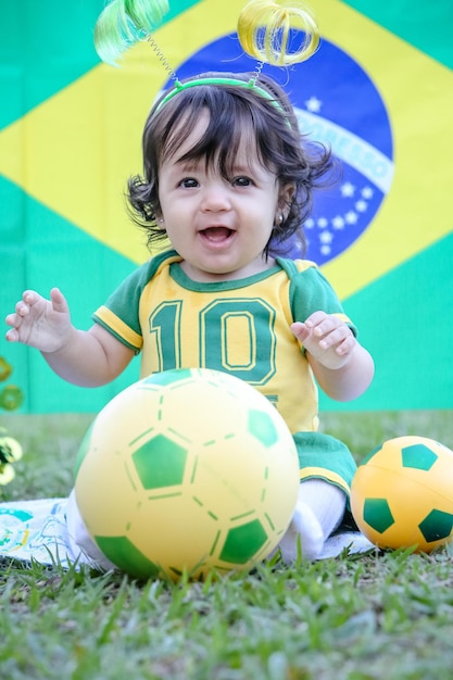 Piękne dziecko brazylijskiej drużyny piłkarskiej w parku, ubrane w zielono-żółto