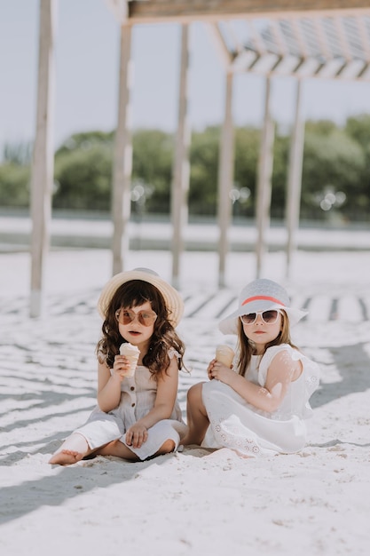 Piękne Dziewczynki W Białej Sukni I Kapeluszu Jedzą Lody Na Plaży W Okresie Letnim