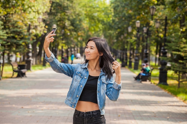 Piękne emocjonalne Azjatki ze smartfonem w dłoniach robienia sobie zdjęć