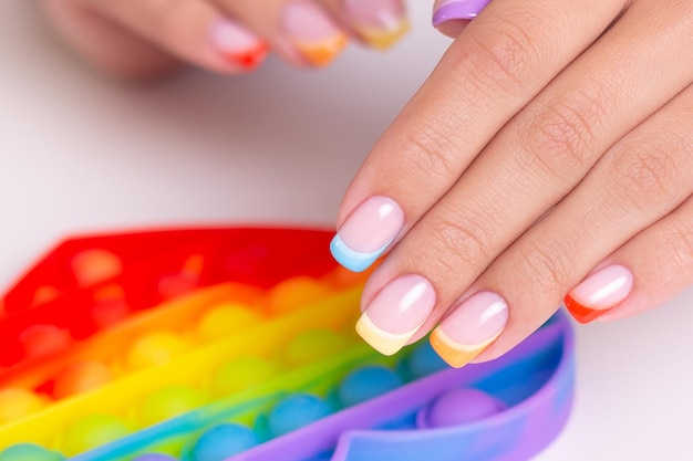 Piękne kobiece dłonie z kolorowymi paznokciami do manicure trzymające zabawkę, pop it