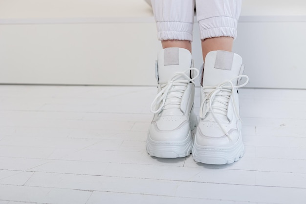 Piękne kobiece nogi w białych spodniach, białe skórzane trampki. Nowa kolekcja damskich butów casual