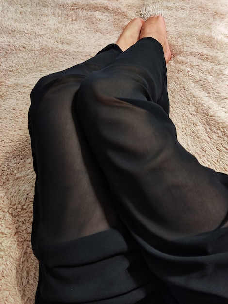 Piękne kobiece nogi w jasnych jedwabnych czarnych spodniach leżą na łóżku na miękkim puszystym beżowym kocu