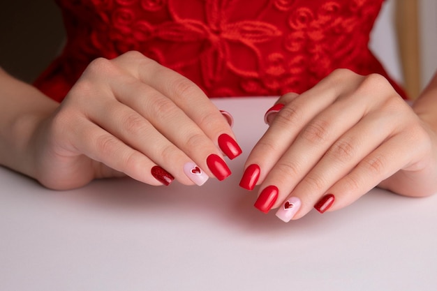 Zdjęcie piękne kobiece ręce z czerwonym manicure, paznokcie, serce i design na walentynki.