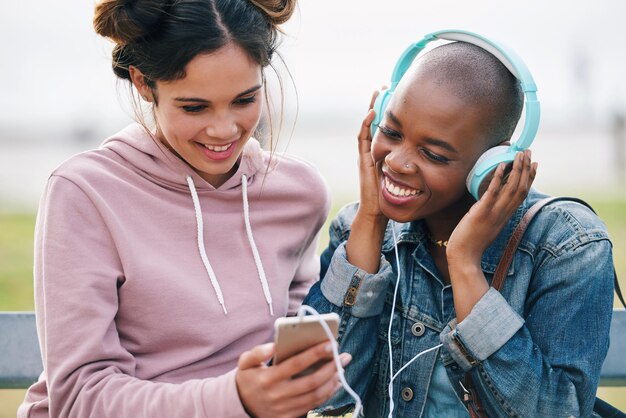 Piękne kobiety przyjaciółki za pomocą smartfona do słuchania muzyki na telefonie komórkowym w słuchawkach spędzających razem czas na świeżym powietrzu