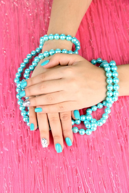 Piękne kobiety ręce z niebieskim manicure trzymając koraliki na koloru tle