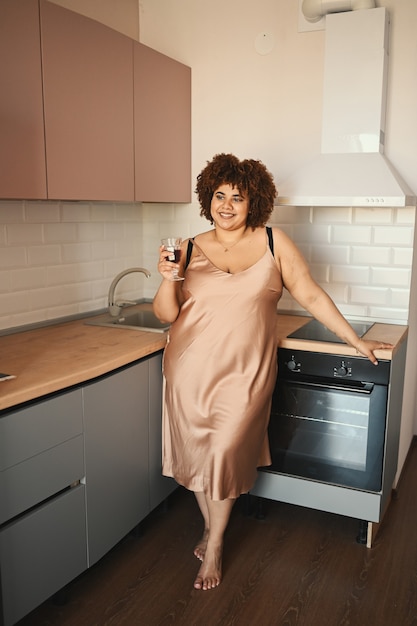 Piękne krągłe plus size afrykańska czarna kobieta z włosami afro pijąca czerwone wino na nowoczesnym skandynawskim