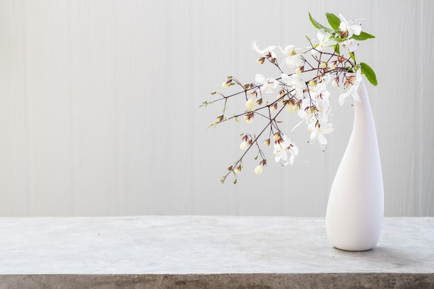 Piękne kwiaty w nowoczesnym wazonie na betonowym stole z białym drewnianym tłem z miejscem na kopię, martwa natura z delikatnym tonem