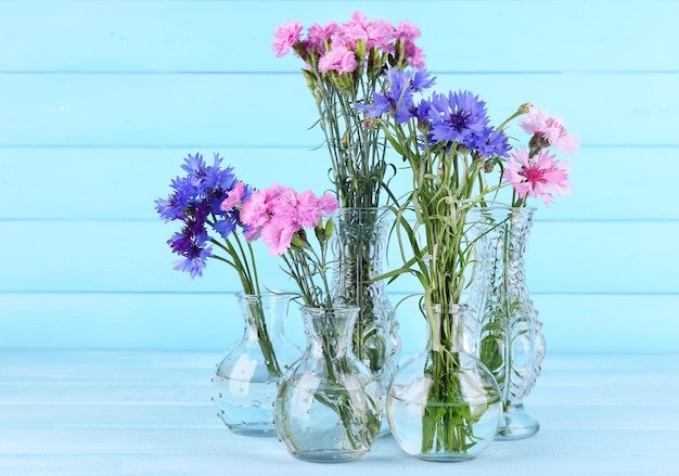 Piękne letnie kwiaty w wazonach na niebieskim drewnianym tle