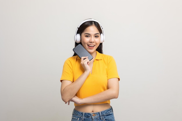 Piękne młode Azjatki wybierają piosenkę i odtwarzają muzykę z połączenia smartfona z bezprzewodowymi słuchawkami, bawiąc się w domu. Nastoletnia dziewczyna słuchać muzyki cieszyć relaks na na białym tle.