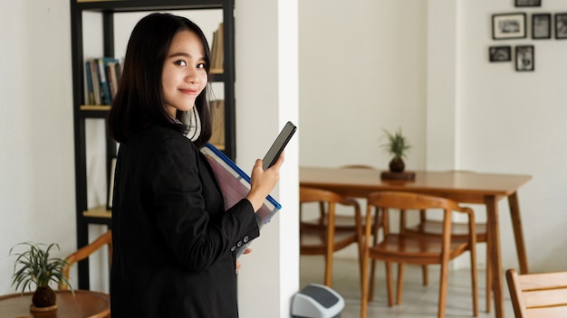 Piękne młode azjatyckie biznes kobieta w garniturze stojącego w kawiarni z telefonem i brązową kopertą