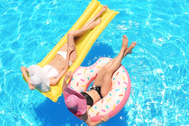 Piękne młode dziewczyny z nadmuchiwanym pączkiem i materacem w niebieskim basenie