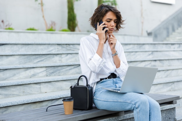 Piękne Myśli Kobieta Siedzi Na Zewnątrz Przy Użyciu Komputera Przenośnego Rozmawia Przez Telefon