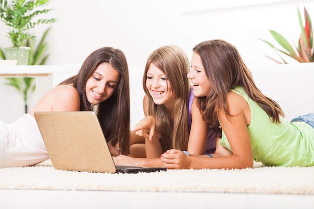 Piękne nastolatki leżące na dywanie z laptopem i surfowanie w internecie.