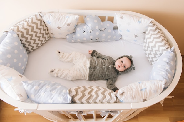 Piękne noworodek leżący w owalnym łóżku z pięknymi zderzakami w delikatnych odcieniach szarości, błękitu i bieli