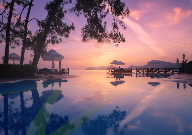 Piękne odbicie w basenie o kolorowym zachodzie słońca Purpurowe niebo odbite w wodzie palmy leżaki parasole w nocy latem Luksusowy kurort Oludeniz Turcja Krajobraz z pustym basenem