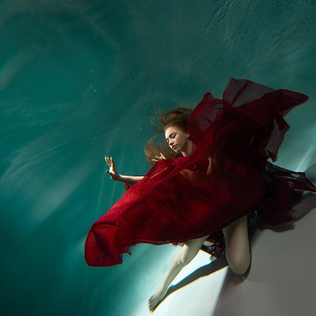 Piękne podwodne fotografowanie młodej kobiety w czerwonej sukience