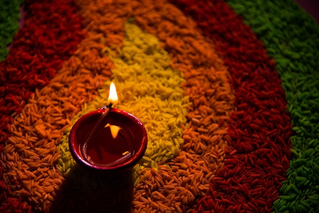 Piękne powitanie Diwali z lampą oliwną Diya lub glinianą zapaloną i ułożoną nad Rangoli z wielobarwnych ziaren ryżu, selektywne skupienie