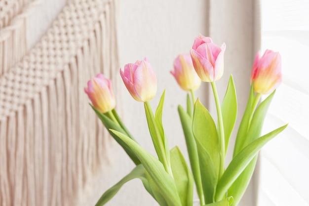 Piękne różowe tulipany na tle ręcznie robionej makramy na ścianie Przyjazna dla środowiska nowoczesna koncepcja we wnętrzu