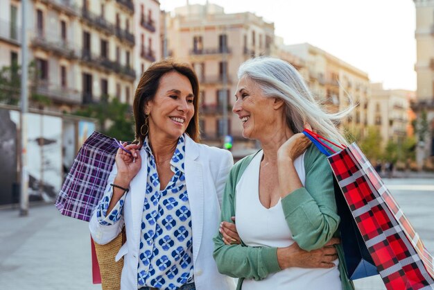 Piękne starsze kobiety łączą się na świeżym powietrzu w mieście. Atrakcyjne, wesołe dojrzałe przyjaciółki bawią się na zakupach i łączą koncepcje dotyczące stylu życia starszych osób