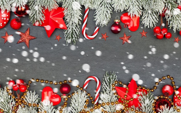 Piękne świąteczne tło. Kolorowa kompozycja z czerwonymi jagodami ostrokrzewu, złotą girlandą, zieloną gałęzią jodły i szklanymi bombkami na czarnym tle ze śniegiem