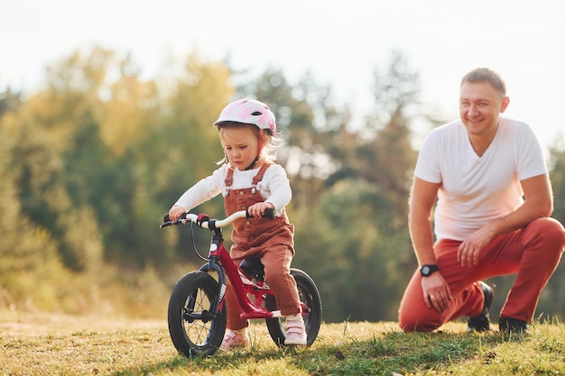 Piękne światło słoneczne Ojciec w białej koszuli uczy córkę, jak jeździć na rowerze na świeżym powietrzu