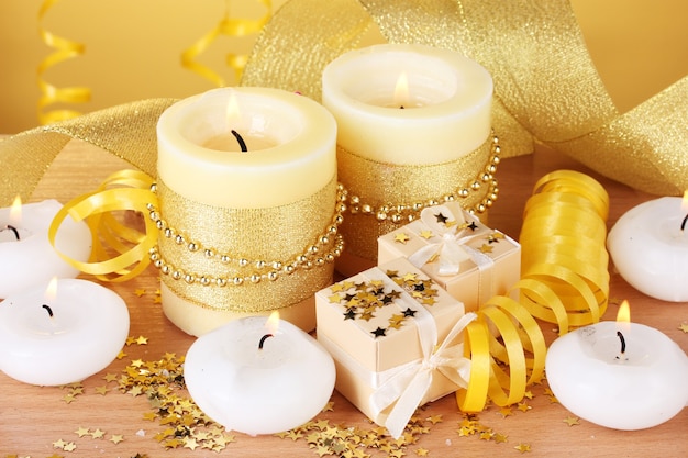 Piękne świece, prezenty i dekoracje na drewnianym stole na żółtym tle