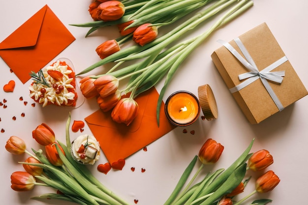 Piękne wiosenne tło, płonące świece, czerwone tulipany, pudełko z prezentami i ciasto.