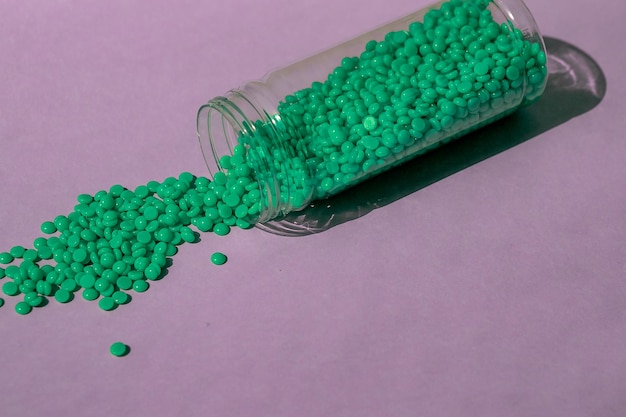 Piękne zielone granulki wosku z ekstraktem z aloesu do depilacji wylewa się na jasnofioletowe tło z przezroczystego słoika Depilacja Depilacja usuwanie niechcianych włosów na tekst