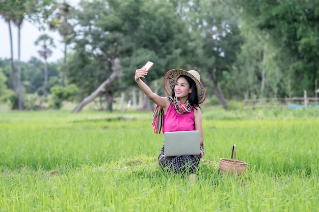 Pięknej azjatykciej kobiety pracujący laptop outdoors w ryżowych polach.