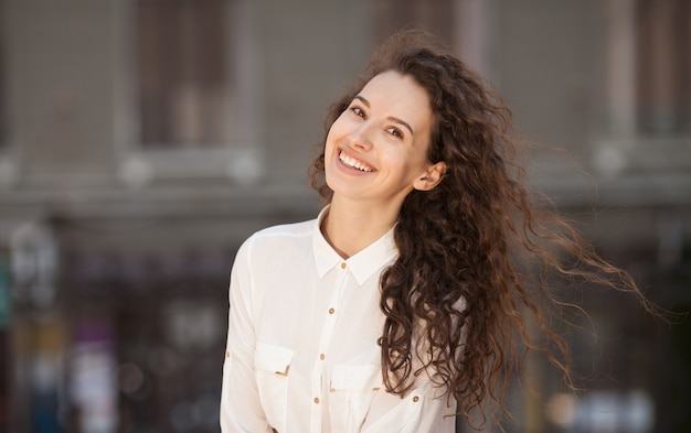 Pięknej brunetki kędzierzawa kobieta ono uśmiecha się outdoors