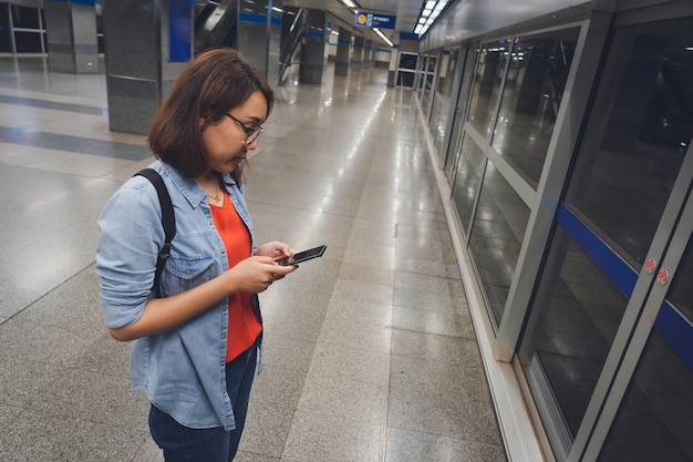 Zdjęcie piękni młodzi turyści stoi czekanie dla metra wraz z używać mądrze telefony