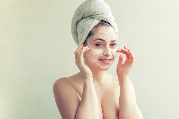 Piękno portret kobiety w ręcznik na głowie z białą odżywczą maską lub kremem na twarzy, na białym tle. Pielęgnacja skóry oczyszczająca eco organiczna kosmetyczna koncepcja spa relaks