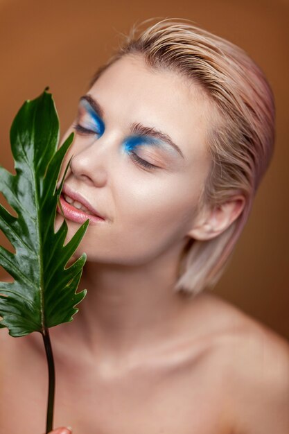 Piękno portret młodej kobiety blondynka z doskonałej skóry moda makijaż i zielony liść na naturalnym brązowym tle. Oczyszczający eco kosmetyk organiczny relaks i koncepcja pielęgnacji skóry. Spa i wellness.