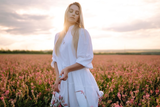Piękno romantyczna dziewczyna Na zewnątrz o zachodzie słońca Młoda kobieta w stylowych ubraniach pozowanie w kwitnącym polu