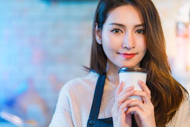Piękny, atrakcyjny azjatycki właściciel sklepu z kawiarnią, uśmiechnięty ze szczęścia i radosny z filiżanką w fartuchu kawiarnianym tle