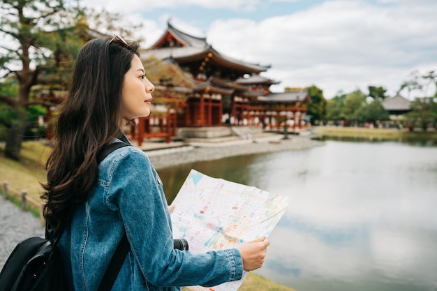 piękny azjatycki podróżnik stojący nad stawem, trzymający mapę i patrzący na widok. Podróży Japonia letnie wakacje dziewczyna korzystających z zwiedzania w Kioto. Szczęśliwy turysta w słonecznej świątyni w Japonii.