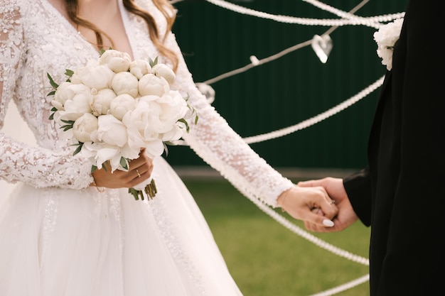 Piękny biały ślubny bukiet piwonii w rękach panny młodej