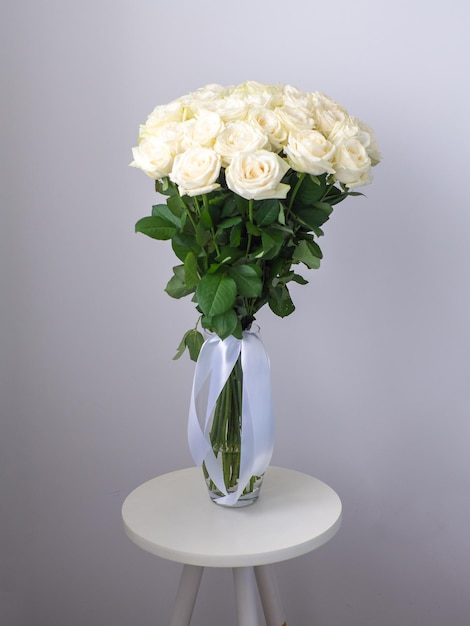 Piękny bukiet białych kwitnących róż w szklanym wazonie na okrągłym stole