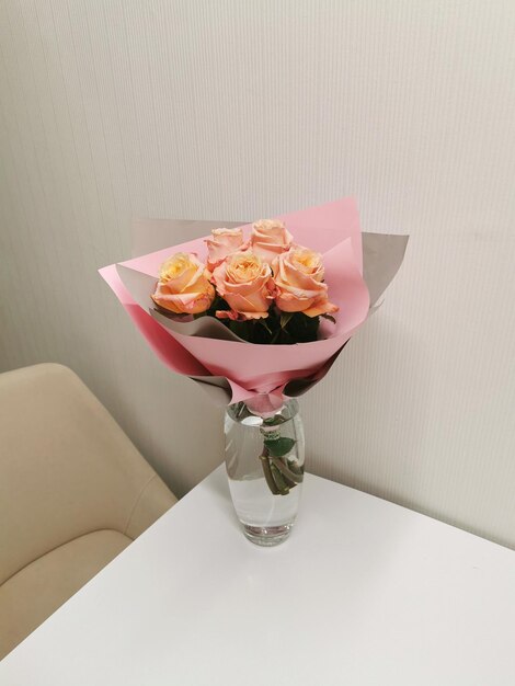 Piękny bukiet brzoskwinioworóżowych róż w różowym opakowaniu w szklanym wazonie na białym stole i wnętrzu Minimalistyczna aranżacja z kwiatami