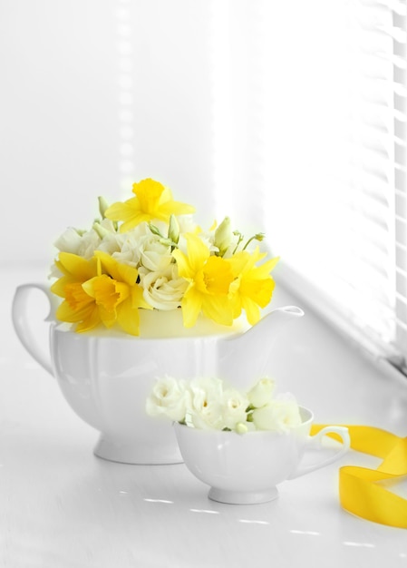 Piękny bukiet żółtych żonkili i róż w czajniczku na parapecie